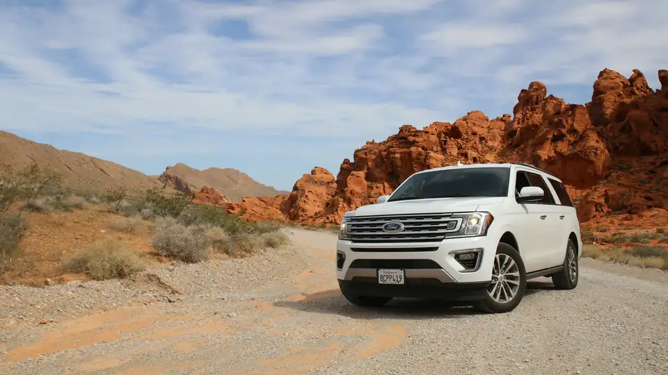 A white SUV parked on a desert road beneath red rocks